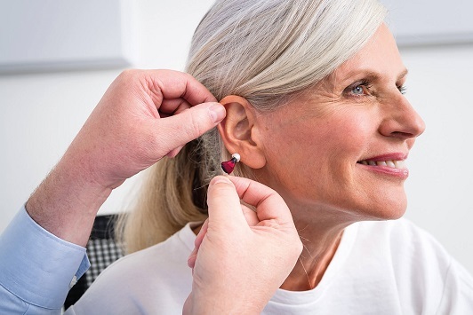 Ältere Frau erhält von einem Hörakustiker ein modernes Hörgerät für besseres Hören.